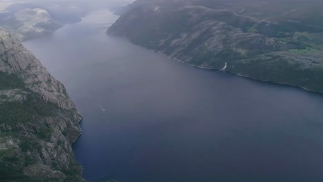 Aerial-Slomo-Titlting-Up-revealing-a-Norwegian-Fjord-close-to-the-Preikestolen-with-Clouds-and-Fog-in-the-background