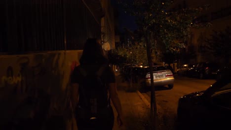Folgende-Aufnahme-Einer-Jungen-Asiatischen-Frau,-Die-Nachts-In-Athen-Eine-Dunkle-Straße-Entlang-Geht