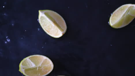 Fresh-slices-of-green-lime-fruit-dropping-into-water-in-pieces-with-splashes-in-slowmotion