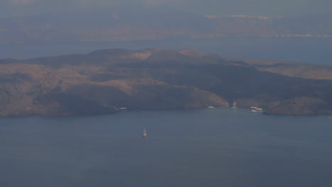 A-ship-is-spotted-near-the-volcanic-island-of-Nea-Kameni,-as-seen-from-the-cliffs-of-the-island-of-Santorini