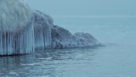 Kleine-Wellen,-Die-An-Einem-Bewölkten-Wintertag-Gegen-Die-Ruinen-Der-Nördlichen-Festung-Karosta-An-Der-Küste-Der-Ostsee-Brechen,-Bedeckt-Mit-Eis,-Schnee-Und-Eiszapfen,-Mittlere-Nahaufnahme