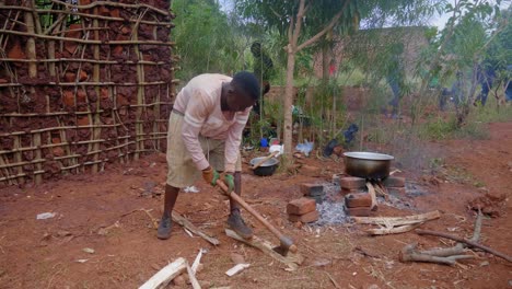 A-wide-shot-of-a-young-African-man-chopping-fire-wood-with-an-axe-in-a-rural-African-village