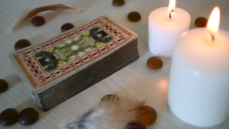 time-lapse-of-a-background-with-mystic-cards-deck-near-candles-with-flickering-flames,-stones-and-feathers