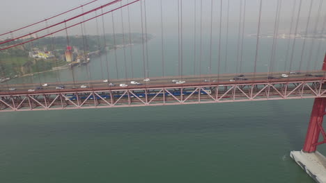 Seitliche-Aufnahme,-Die-Einem-Zug-Unter-Der-Lissabon-Brücke-Vom-25.-April-In-Portugal-Folgt