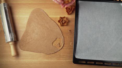 Making-shapes-from-gingerbread-dough-on-a-wooden-table-and-placing-them-to-baking-tin-topdown-video