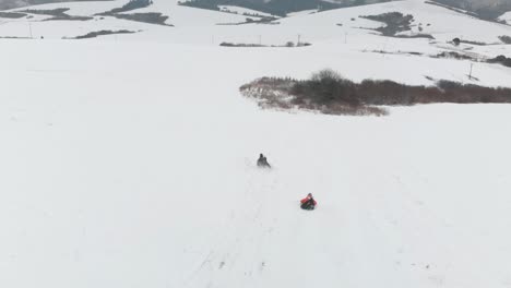 Luftaufnahme,-Menschen-Auf-Holzschlitten-Fahren-Bergab-In-Winterlicher-Schneelandschaft-Mit-Dorf-Im-Hintergrund