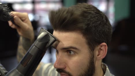 Young-handsome-bearded-man-is-combing-his-hair-with-comb-and-hairdryer