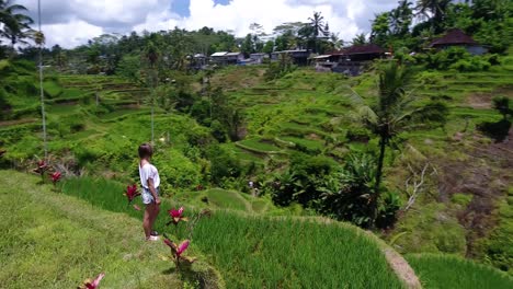 Drone-circle-shot-around-a-beautiful-young-woman-standing-on-the-edge-of-a-rice-terrace-in-Ubud-on-Bali,-Indonesia