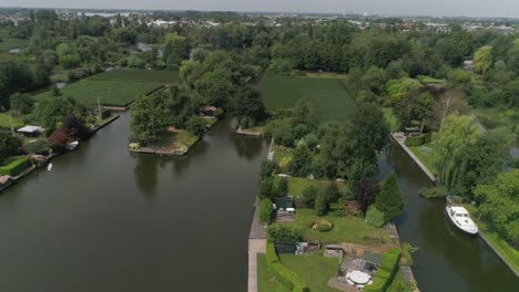 Aerial-Slomo-of-Dutch-Countryside-surrounded-with-Small-Rivers,-Green-Trees-and-Bushes,with-Small-Town-in-background