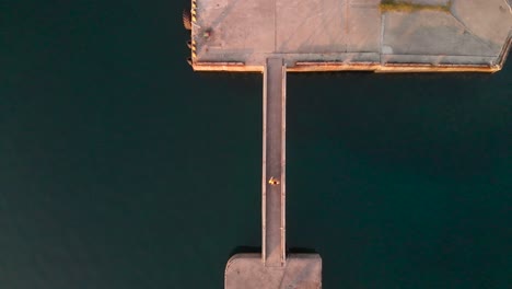 Vista-Aérea-De-Drones-De-Arriba-Hacia-Abajo-De-Un-Hombre-Caminando-Por-Un-Puente-De-Piedra-En-El-Puerto-Oceánico