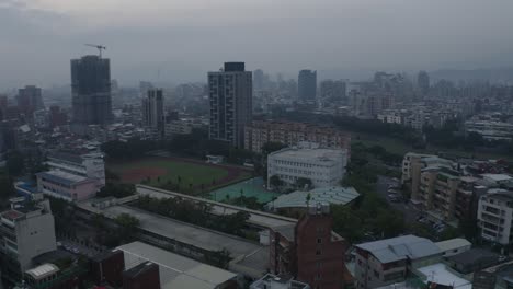 A-drone-shot-of-Taipei,-revealing-kids-playing-baseball-on-a-school-field