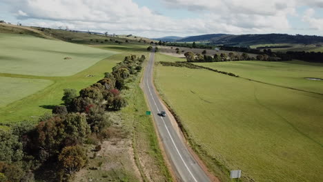 Drone-Shot-Of-Car-Driving-Off-Into-Distance-Along-Straight-Country-Road-Lined-By-Trees