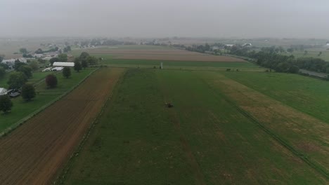 Drone-Ariel-View-of-Amish-Farm-Lands-and-Amish-Farmer-Harvesting-in-Fog