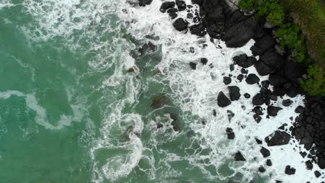 Beach,-blue-ocean,-waves-and-black-rocky-coast---Top-Down---Aerial-Drone