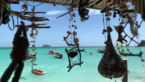 A-shot-of-multiple-wind-chimes-hanging-and-facing-to-the-ocean-with-Thailand-long-tail-boats-and-blue-sky-in-the-background