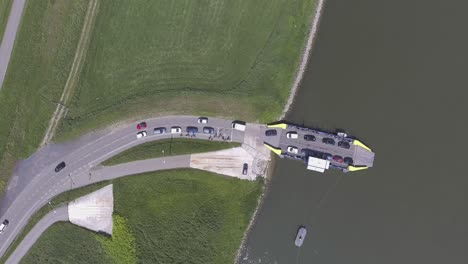 Eine-Von-Oben-Nach-Unten-Gerichtete-Drohnenaufnahme-Einer-Fähre,-Die-Autos-Und-Menschen-Von-Einem-Fluss-Zum-Land-Lädt,-Nach-Unten-Geschwenkt,-In-Den-Niederlanden