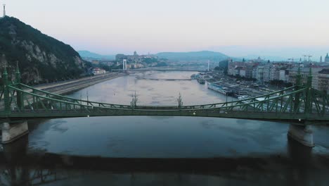 Aerial-view-of-Liberty-bridge-on-river-Danube-in-Budapest-at-sunrise,-morning,-backward-movement