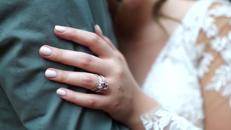Close-up-of-wedding-ring-on-finger-of-bride-holding-grooms-arm