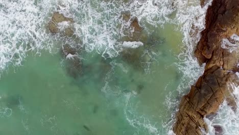 Aerial-drone-shot-looking-straight-down-and-moving-backwards-over-the-rocks-and-surf