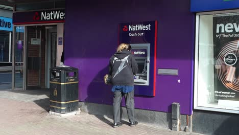 A-woman-using-an-Natwest-ATM,-cash-machine-to-withdraw-money,-deposit-cash-or-pay-some-bills-on-the-high-street-in-the-city-centre