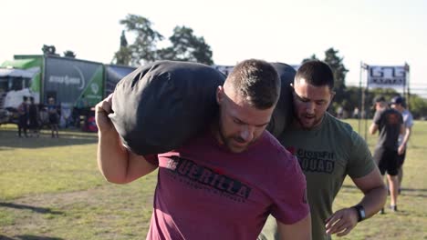 young-fit-athletic-men-doing-weighted-lunges-with-a-heavy-bag-together-as-a-team-during-a-cross-fit-competition-on-a-hot-sunny-day