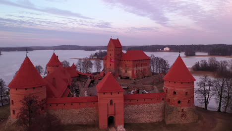 Luftaufnahme:-Abschluss-Einer-Drohnenaufnahme-Der-Mittelalterlichen-Inselburg-Trakai-Im-Gotischen-Stil-Mit-Violettem-Abendlicht,-Das-Vom-Sonnenuntergang-An-Die-Wände-Fällt