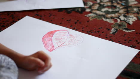 Kleines-Mädchen-Zeichnet-Ein-Lila-Herz-Auf-Ein-Blatt-Papier-Im-Haus