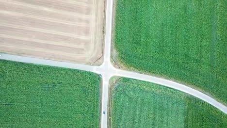 A-single-car-driving-on-a-crossroad-with-green-fields,-drone-helicopter-view-perfect-square-plus-shape
