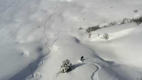 Aerial-view-tracking-a-snowboarder-from-above,-off-piste-in-fresh-snow,-in-the-French-Alps-in-winter