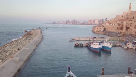 Jaffa-Hafen-Mit-Fahrenden-Booten,-Die-Mauerwerksarchitektur-Und-Mittelalterlichen-Einfluss-Zeigen,-Während-In-Der-Ferne-Die-Moderne-Skyline-Von-Tel-Aviv-Etwa-Im-März-2019-Zu-Sehen-Ist