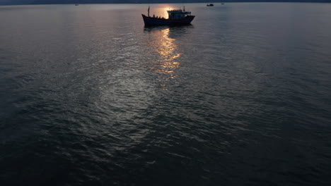 Reveal-shot-of-a-beautiful-Vietnamese-landscape-of-ocean,-mountains-and-a-silhouette-of-a-traditional-fishing-boat-docked-at-sunset