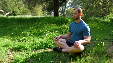 Ein-Mann-Sitzt-In-Einer-Meditationspose-In-Einem-Grünen,-Sonnigen-Wald-Und-übt-Tiefe-Atemübungen,-Um-Stress-Abzubauen-Und-Achtsamkeit-In-Zeitlupe-Zu-Trainieren