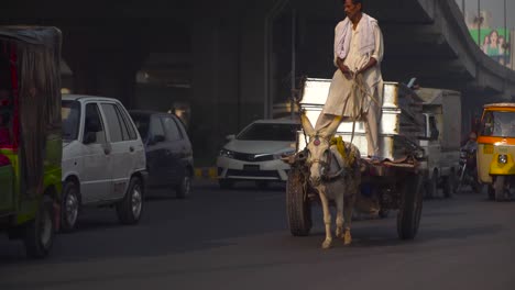 A-donkey-car-is-going-on-the-road,-Traffic-close-up-at-the-road-under-the-fly-over,-passing-motor-bikes-and-cars,-Buses,-rickshaw`s,-Billboards-and-buildings-in-the-background