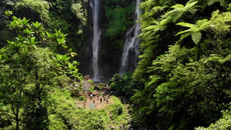 Drone-footage-of-a-crowd-of-people-taking-pictures-in-front-of-an-amazing-water-fall,-deep-in-a-green-forest