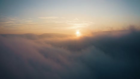 Rising-above-clouds-at-sunset-with-clouds-and-mystic-fog,-aerial-drone-shot