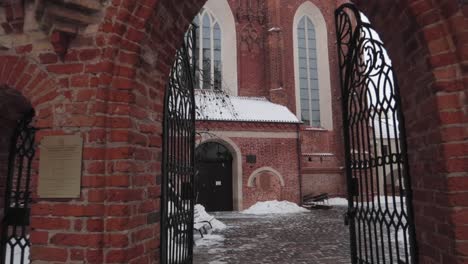 Dolly-in-shot-of-a-red-brick-church-courtyard-passing-through-gate-walking-forward