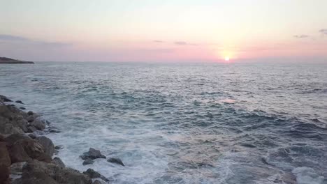 Wellen-Rollen-Langsam-über-Die-Felsen-Des-Wellenbrechers-Im-Hafen-Von-Jaffa,-Während-Ein-Wunderschöner-Sonnenaufgang-In-Rosa-Und-Gelb-Den-Himmel-Erfüllt