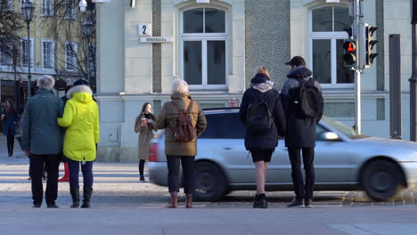 Pedestrians-Wait-at-the-Crosswalk-to-Cross-the-Street-While-Automobiles-Drives-on-Street