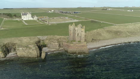 Aerial-shot-backing-away-from-Keiss-Castle-out-towards-the-sea-on-a-sunny-day,-Caithness,-Scotland