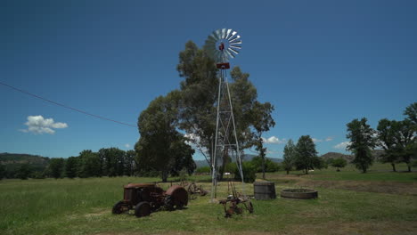 Zeitlupenschwenk-Einer-Windmühle-Auf-Einer-Ländlichen-Ranch-Mit-Einem-Alten-Antiken-Traktor-Im-Vordergrund-In-Nordkalifornien