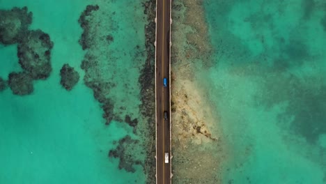 Birds-eye-view-following-car-bridge-over-turquoise-water-on-tropical-island
