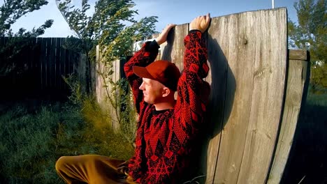 SLOW-MOTION---Male-adult-against-a-fence-in-the-wind-looking-into-the-sunny-wearing-a-black-and-red-sweater