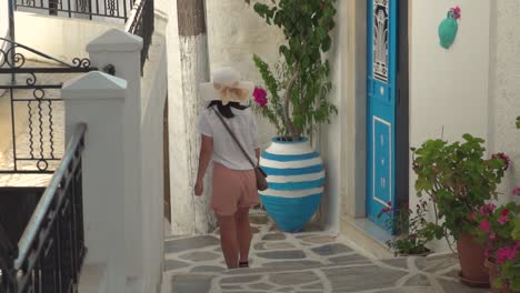 Girl-in-summery-hiking-outfit-walking-through-typical-narrow-Greek-alley-with-blue-doors-and-plants