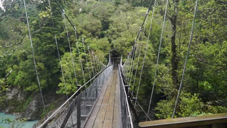 SLOWMO---Swing-Bridge-over-blue-glacier-river-at-Hokitika-Gorge,-South-Island,-New-Zealand
