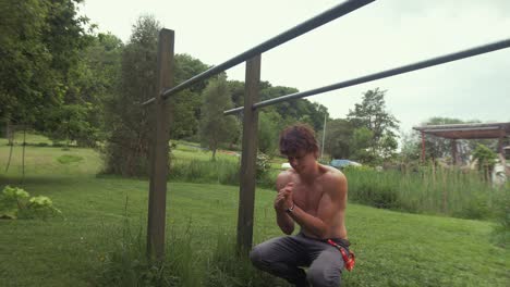 Young-fit-topless-man-stretches-wrists-before-exercising-on-parallel-bars-at-home-gym