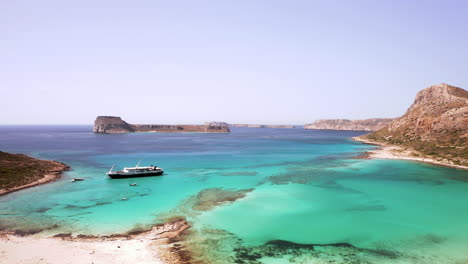Luftvorbeiflug-Eines-Tageskreuzfahrtbootes,-Das-Am-Strand-Von-Balos-Auf-Kreta,-Griechenland,-An-Einem-Schönen-Sonnigen-Tag-Mit-Türkisfarbenem-Wasser-Und-Weißem-Sand-Abfährt