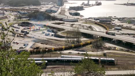 Aerial-clip-of-Freight-train-slowly-moving-along-tracks-amidst-a-busy-highway-in-Uddevalla-Sweden