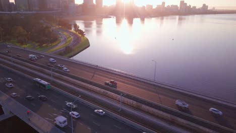 Aerial-view-of-a-narrows-bridge-with-busy-morning-commute,-camera-motion-forward-revealing-Perth-CBD-Skyline-at-sunrise