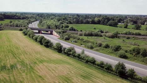 Drone-flying-over-A34-trunk-road-which-is-intersected-by-a-railway-bridge-crossing,-showing-transport-cutting-through-countryside-in-the-UK