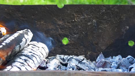 Burning-wood-an-coals-in-rusty-portable-outdoor-BBQ-grill-in-sunny-day,-close-up-shot